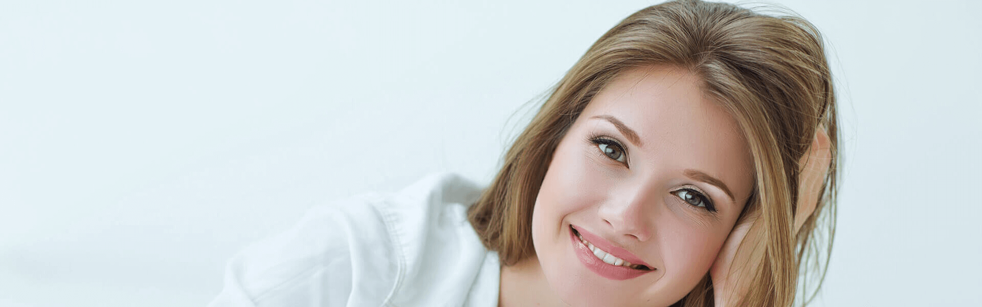 A close-up picture of a smiling woman displaying beautiful dental work done by the top dentists in Costa Rica.  The woman is looking directly at the camera and holding one hand to the side of her head to highlight her perfect teeth.
